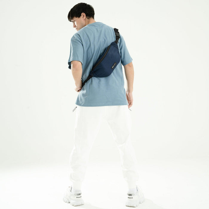 Man wearing blue crossbody fanny pack with adjustable strap, casual outfit, white background