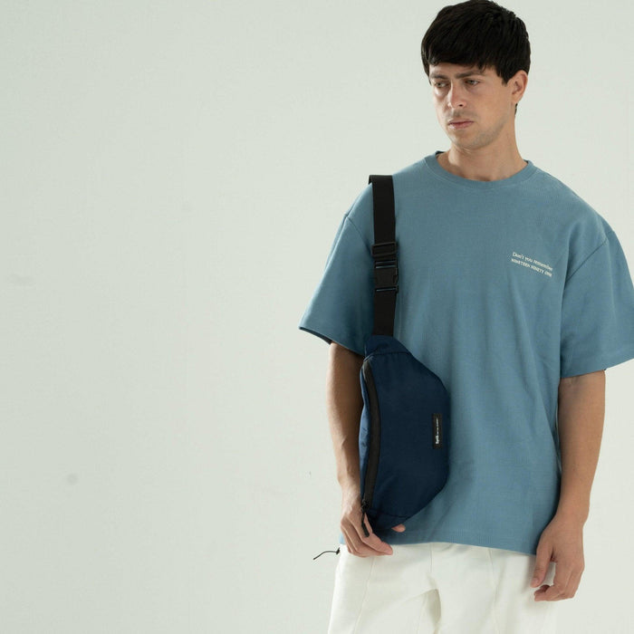 Man wearing blue crossbody waist bag with black strap over blue t-shirt and white pants