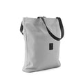 Minimalist light grey shoulder bag with black strap and small logo patch on white background
