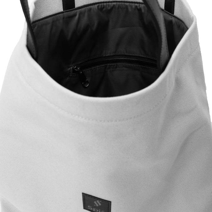 White canvas tote bag with black handles and interior zip pocket, close-up view