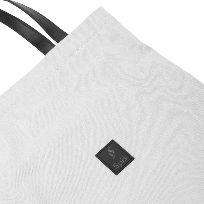 White canvas tote bag with black handles and Spiš logo patch, minimalist design
